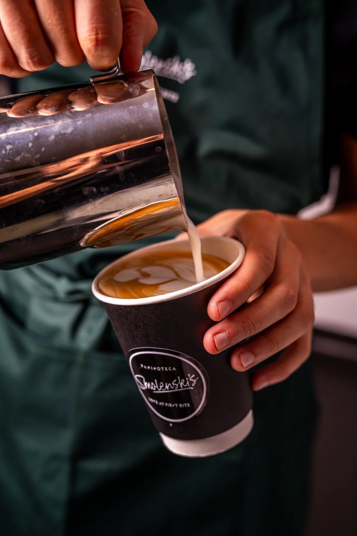 A barista pouring milk into a Smolenski’s takeaway coffee