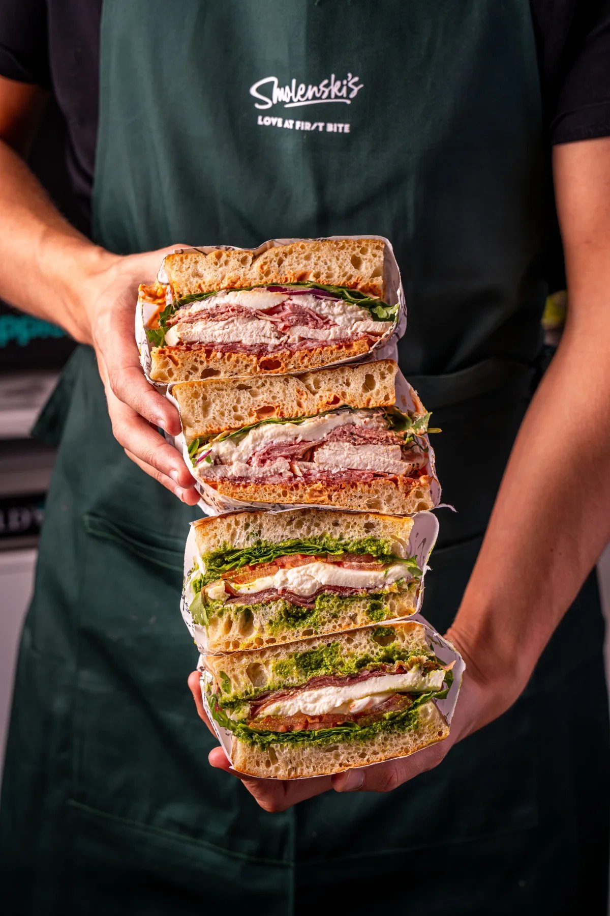A stack of generously filled focaccia sandwiches held by a team member